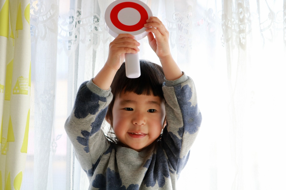 マルの書かれたプレートを両手で掲げた子ども